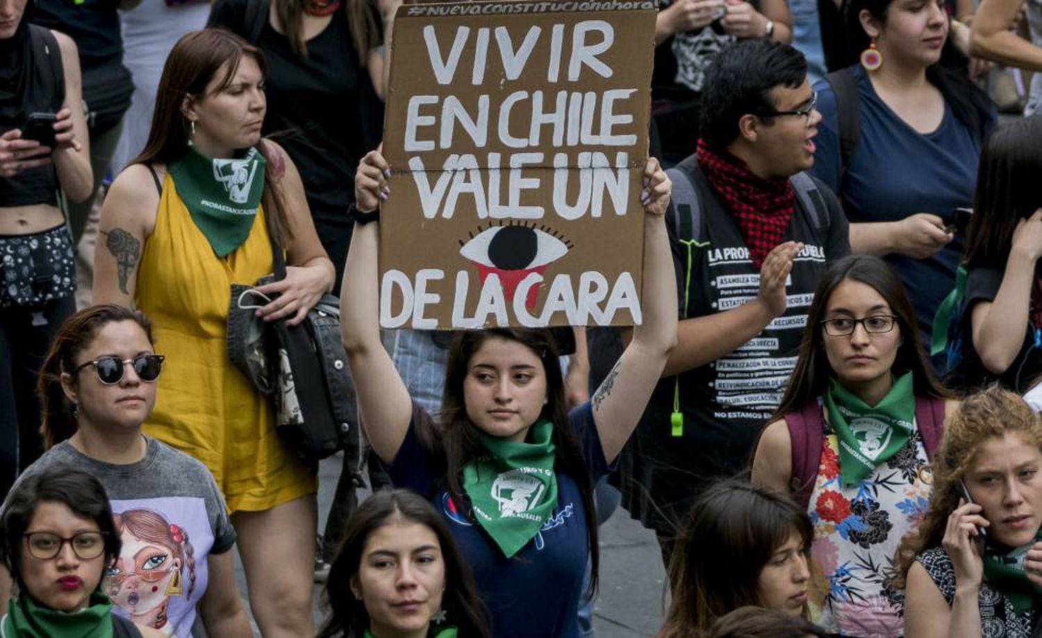Manifestante segura cartaz onde se lê: “Viver no Chile custa o olho da cara”.