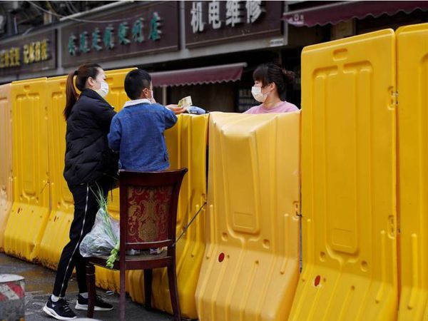 Una mujer paga la compra en un mercadillo delimitado por una barrera, en Wuhan.